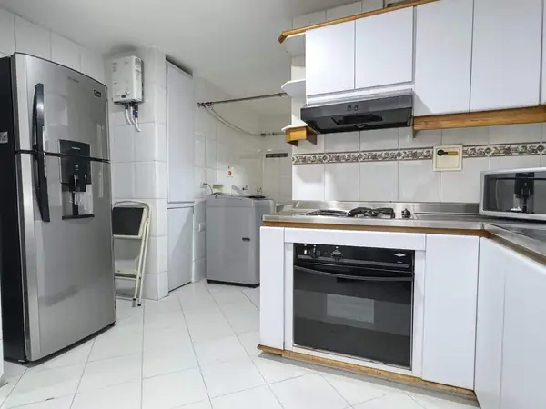 Cocina con nevera de acero inoxidable, horno y lavadora al fondo