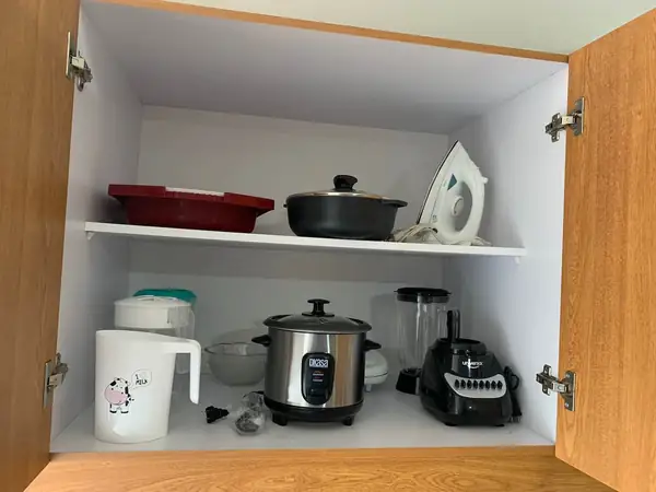 Arrocera, licuadora, ollas y plancha en un gabinete de la cocina