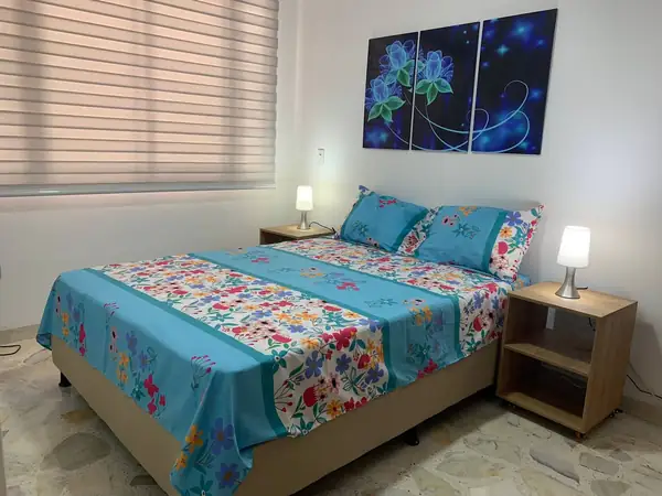 Habitación con cama, mesas de noche y cuadro de flores azules